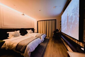 A hotel room with two beds, a large screen, and a wooden floor.