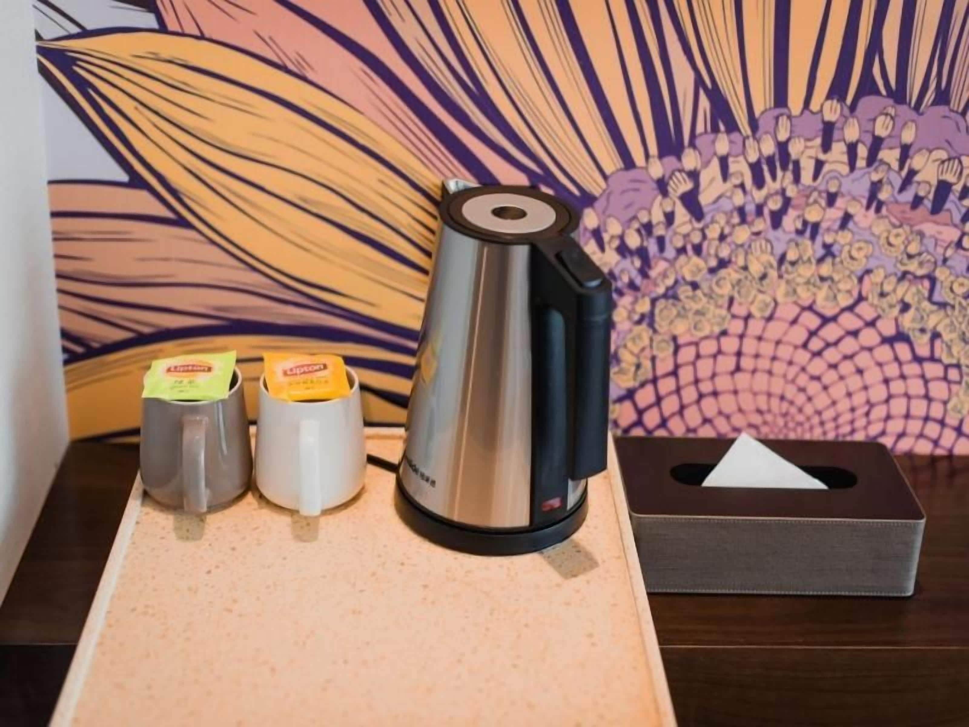 A coffee maker, two cups, and a tissue box on a table with a patterned wall in the background.