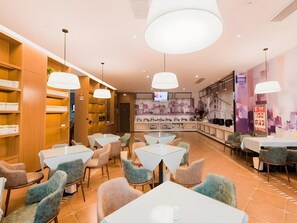 Un intérieur de restaurant moderne avec de nombreuses tables et chaises, un bar et une fresque murale représentant un paysage urbain.