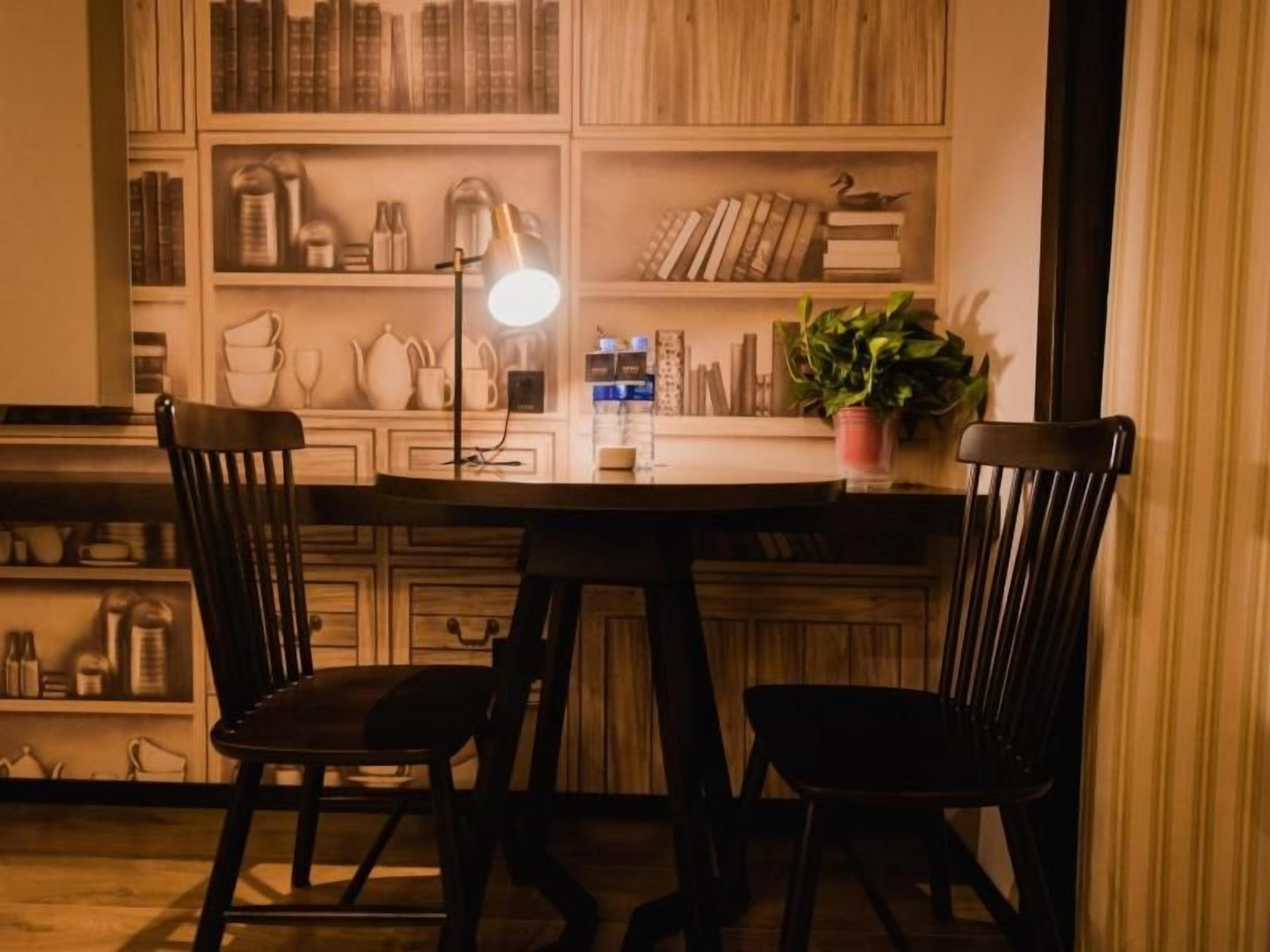 En spiseplads med et bord og to stole, en lampe samt reoler med bøger og pynteting.