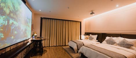 A hotel room with two beds, a large screen, a desk, and a curtain.