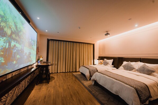 A hotel room with two beds, a large screen, a desk, and a curtain.