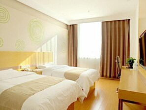 Ett hotellrum med två sängar, ett skrivbord, en spegel och ett fönster med gardiner.