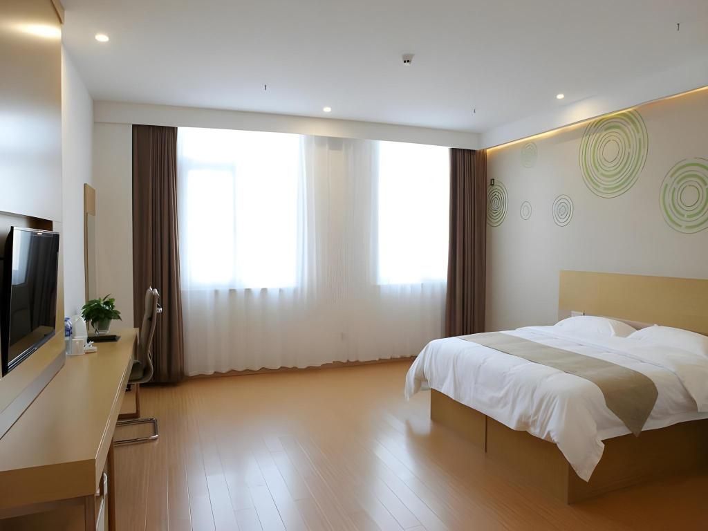 Quarto de hotel com cama, secretária e televisão, e uma janela grande com cortinas.