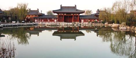 Un edificio tradicional con su reflejo en un cuerpo de agua tranquilo, rodeado de rocas y árboles.