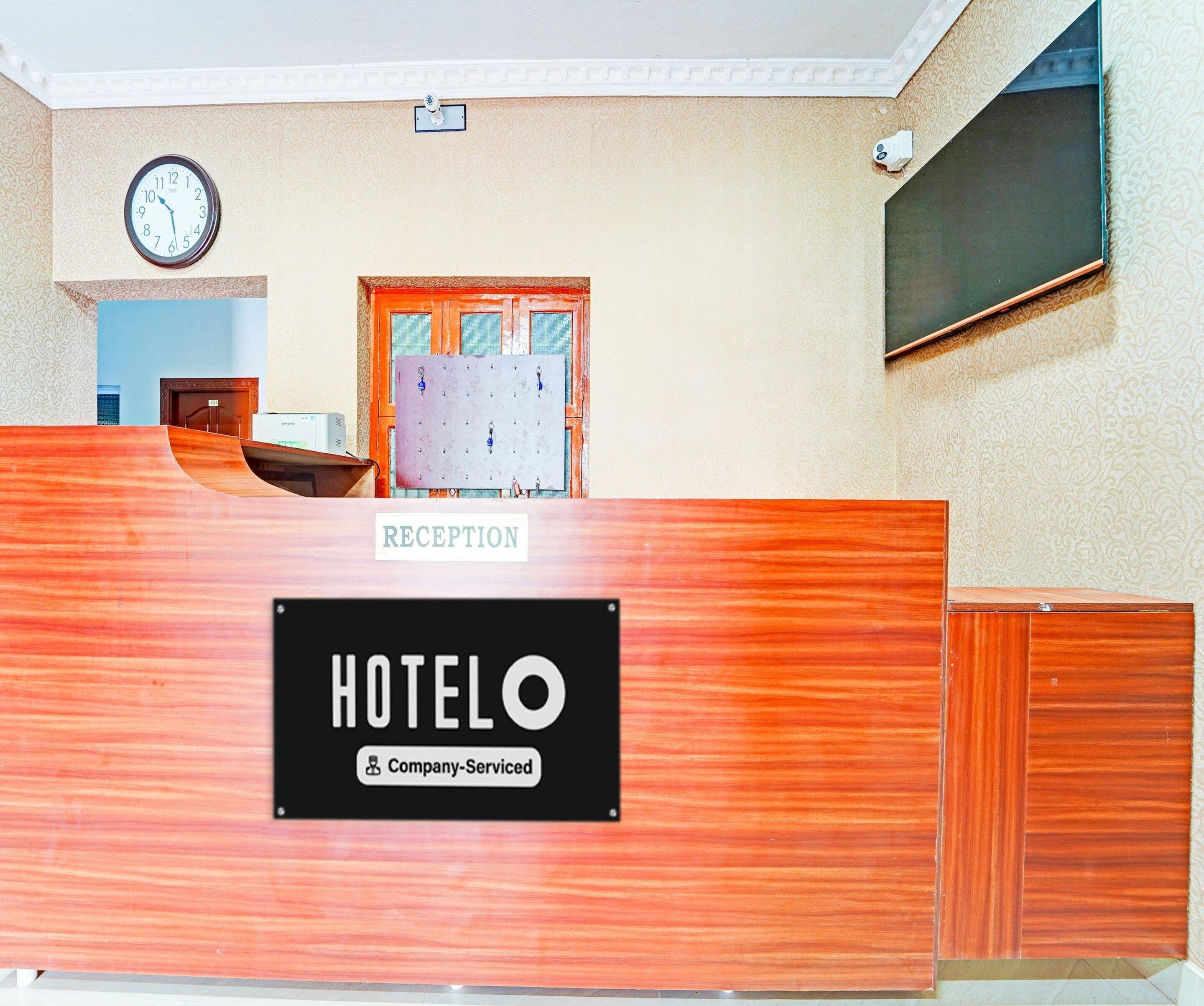 A hotel reception desk with a clock on the wall, a reception sign, and a company-serviced label.