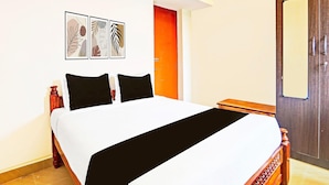 Ein Hotelzimmer mit einem Bett, einem Nachttisch aus Holz, einer Tür und einem an der Wand befestigten Kunstwerk.