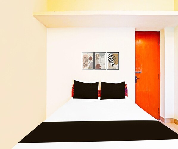Una habitación de hotel con una cama, una puerta roja y tres cuadros en la pared.