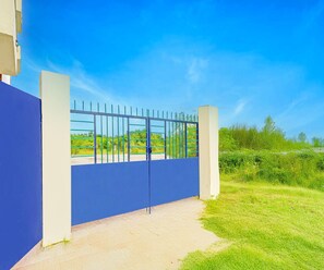 Une entrée fermée par un portail, donnant sur une propriété avec un ciel dégagé et une végétation luxuriante en arrière-plan.
