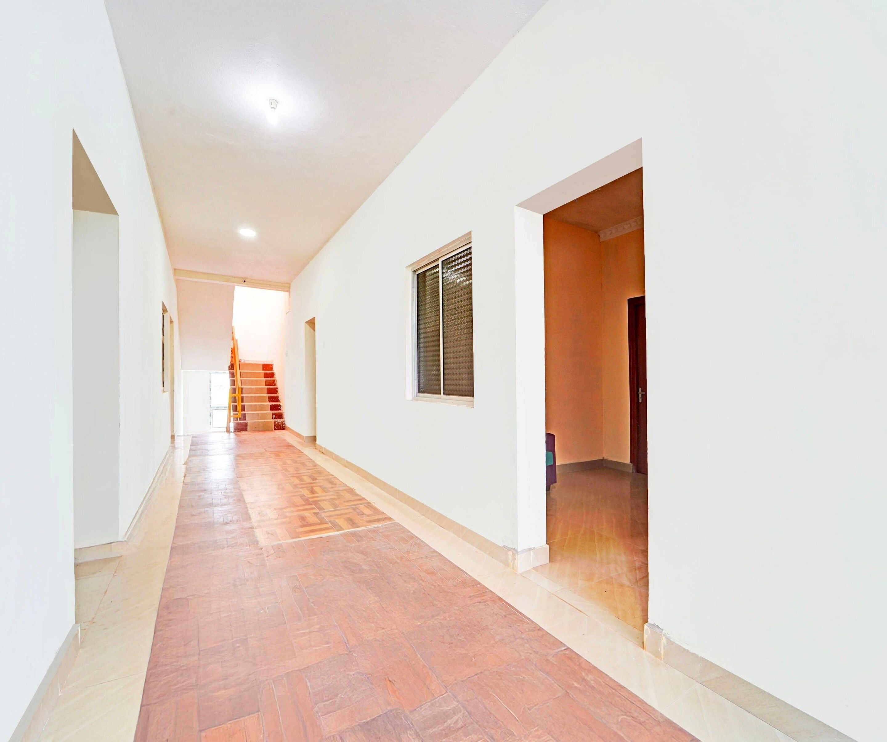 A hallway with a tiled floor, white walls, and a wooden door at the end.