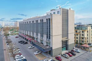A multi-story hotel with a modern facade, a parking lot with several cars, and a clear view of the surrounding cityscape. - Lavande Hotel (Tianjin)