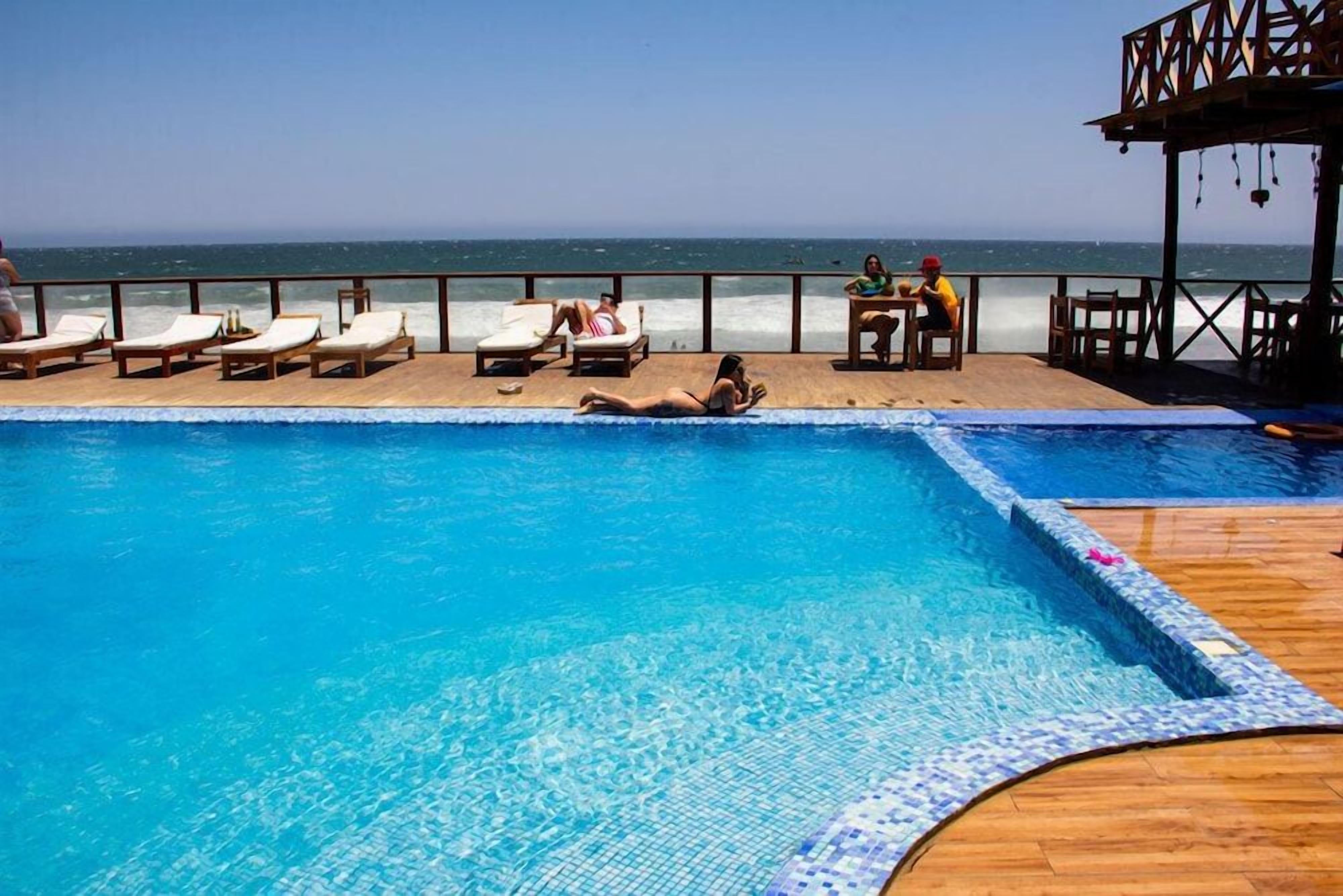 A pool area with lounge chairs and a wooden deck overlooking the ocean.