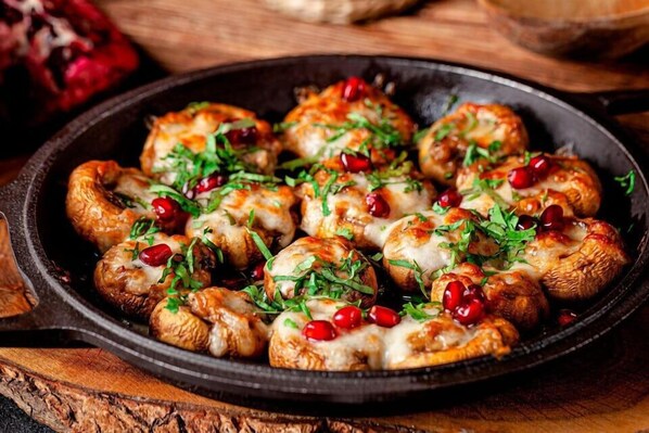 Een koekenpan met geroosterde aardappelen, versierd met kruiden en granaatappelpitjes.