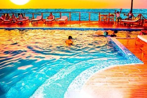 A swimming pool with people relaxing on the deck, surrounded by a wooden railing. - Hotel Costa Blanca de Mancora (Los Organos)