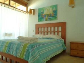 A bed with a striped bedspread, a wooden headboard, and a painting of sailboats on the wall. - Hotel Costa Blanca de Mancora (Los Organos)