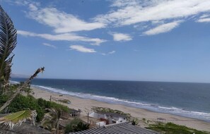 A beach view with a clear sky, a sandy shore, and some buildings in the distance. - Hotel Costa Blanca de Mancora (Los Organos)