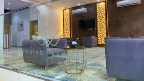 Rebedor modern d'hotel amb separador de vidre, zona de seients amb sofàs, televisió penjada a la paret i aparell d'aire condicionat.