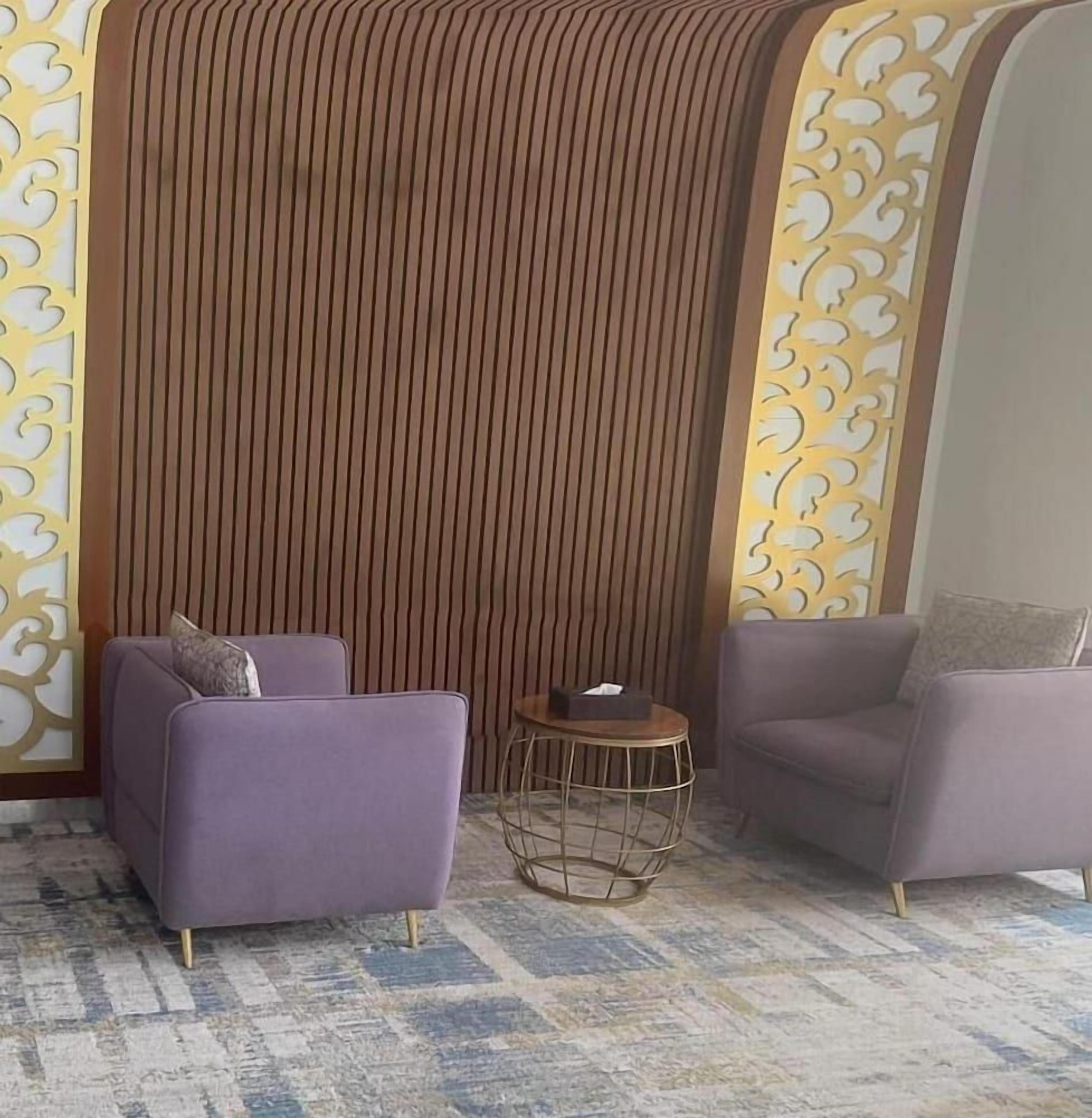 A room with two purple armchairs, a small round table, and a decorative wall with vertical lines.
