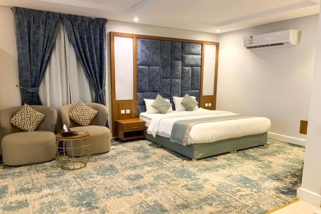 A bedroom with a bed, two armchairs, a side table, and a large window with curtains.