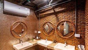 Casa de banho com três lavatórios, um espelho e parede de tijolos.
