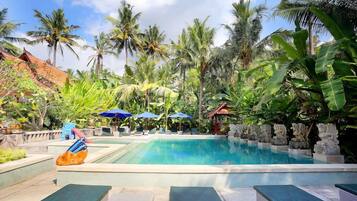 A swimming pool with lounge chairs and umbrellas, surrounded by palm trees and tropical plants.