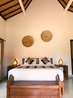 Une chambre d’hôtel avec un lit en bois, deux lampes fixées au mur et deux éléments de décoration murale en fibres tressées.