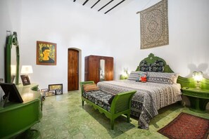 Une chambre à coucher avec un lit, une chaise verte, une armoire en bois et une table de chevet avec une lampe.
