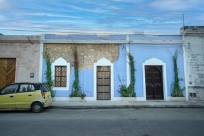 Un bâtiment à la façade bleue, doté de trois portes en arc de cercle et devant lequel est garée une voiture.