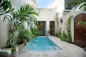 Une piscine entourée de verdure, une porte en bois et un mur en béton.