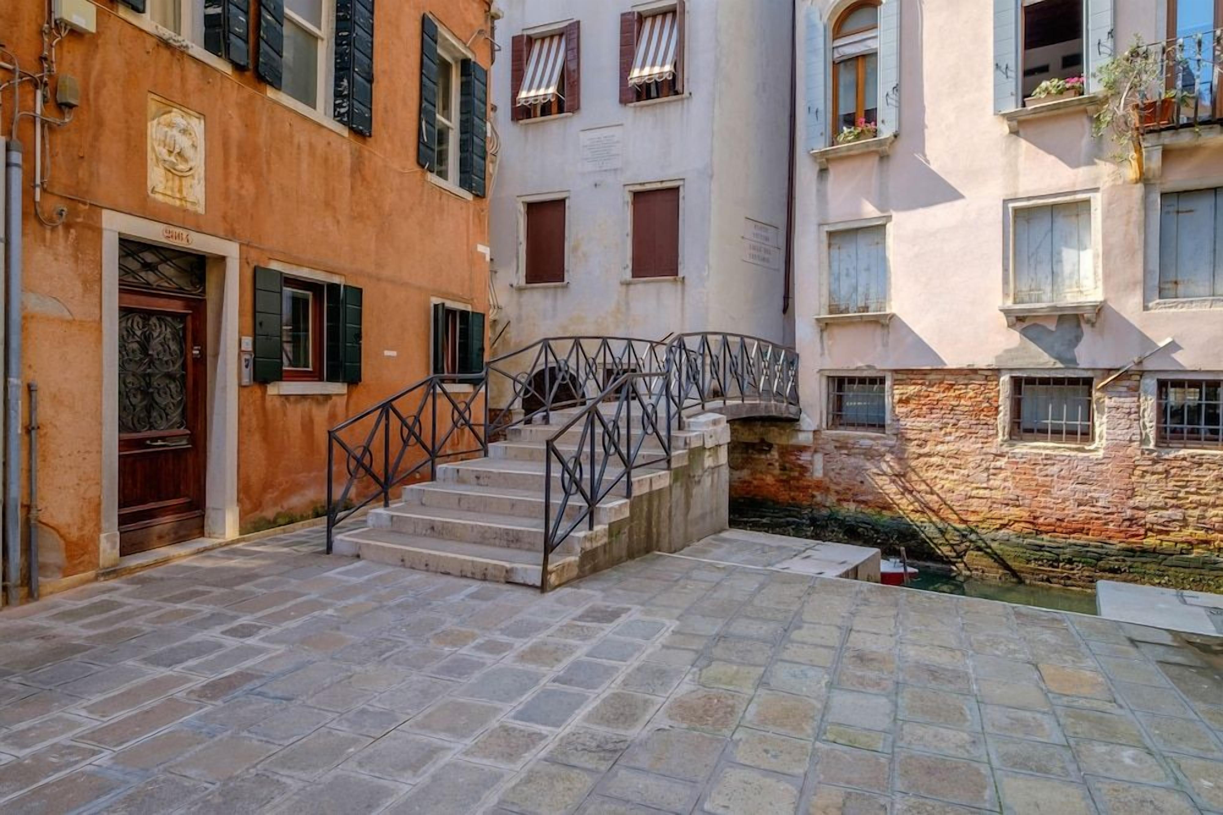 A courtyard with a stone staircase leading to a building entrance, surrounded by buildings with balconies and windows.