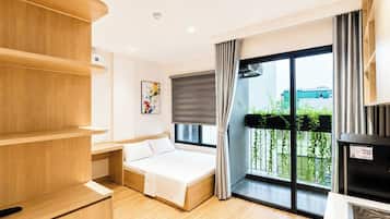 Habitación de hotel moderna con una cama, estanterías de madera, un cuadro, un balcón con vistas y un cubo de basura negro.