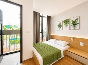 Ein modernes Hotelzimmer mit einem großen Fenster, einem Bett mit grüner Tagesdecke und drei gerahmten Pflanzenbildern an der Wand.