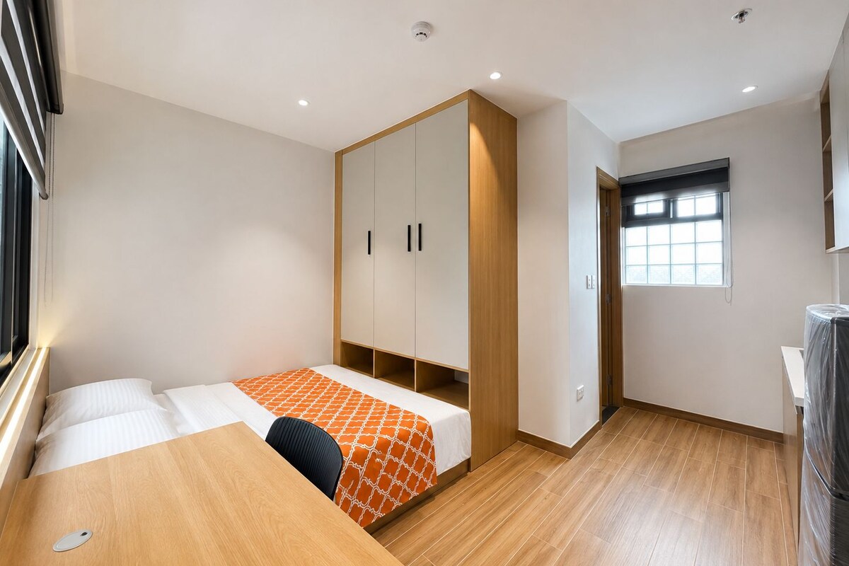 Quarto pequeno e moderno, com uma cama, escrivaninha de madeira e guarda-roupa.