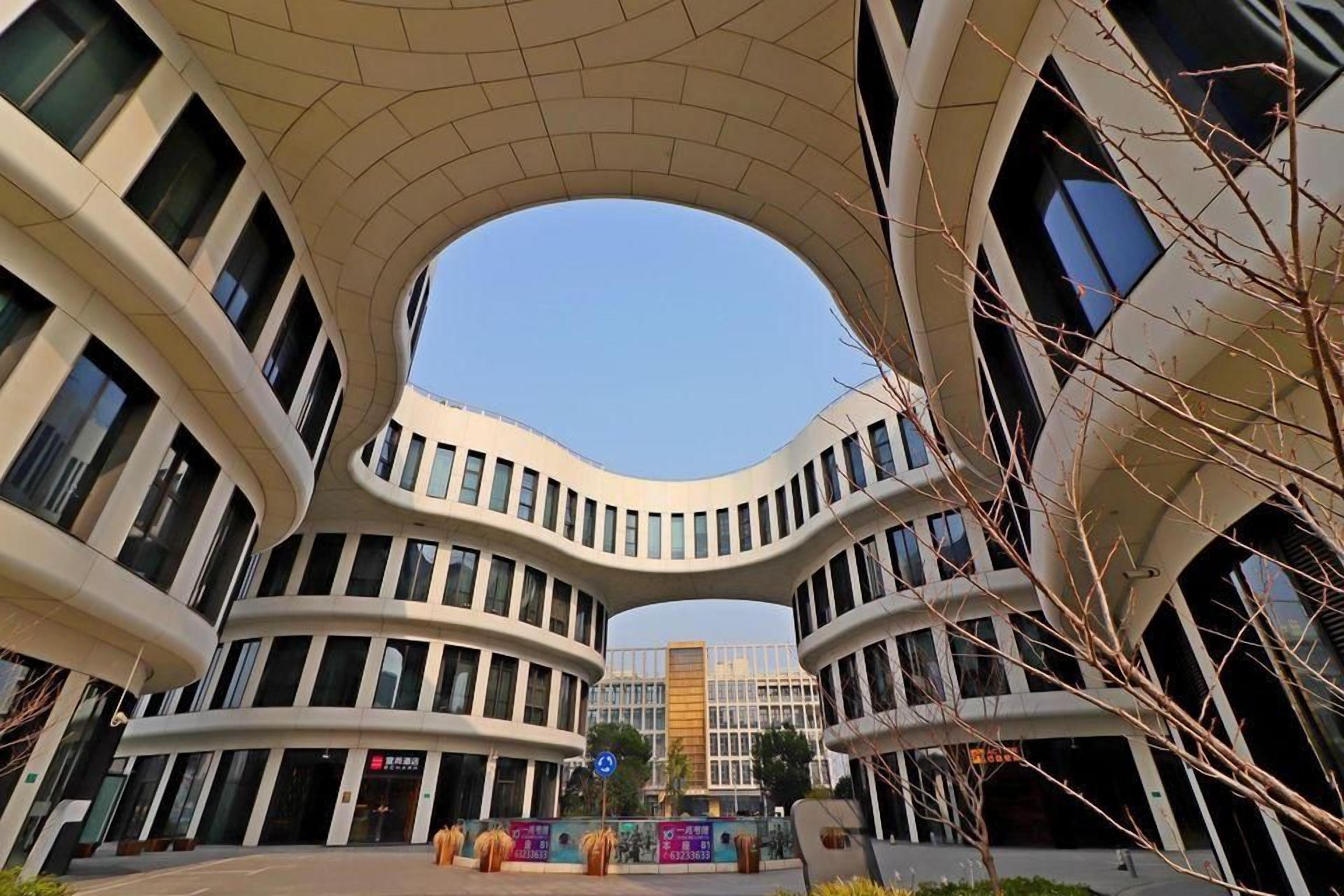 Un bâtiment moderne à la façade incurvée, doté de nombreuses fenêtres, et se dressant sous un ciel dégagé.