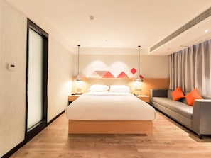 Quarto de hotel com cama, sofá, mesa de cabeceira e parede com padrões geométricos.