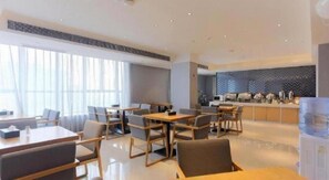 Um saguão de hotel moderno com área de refeições, balcão de recepção e cozinha ao fundo.