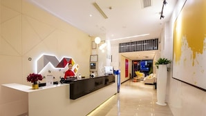 En modern hotellobby med en receptionsdisk, en digital skärm och en sittgrupp med en soffa och stolar.