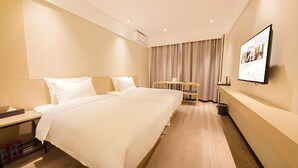 Ett hotellrum med en stor säng, sängbord, ett skrivbord, en stol, en tv som är monterad på väggen och en gardin.
