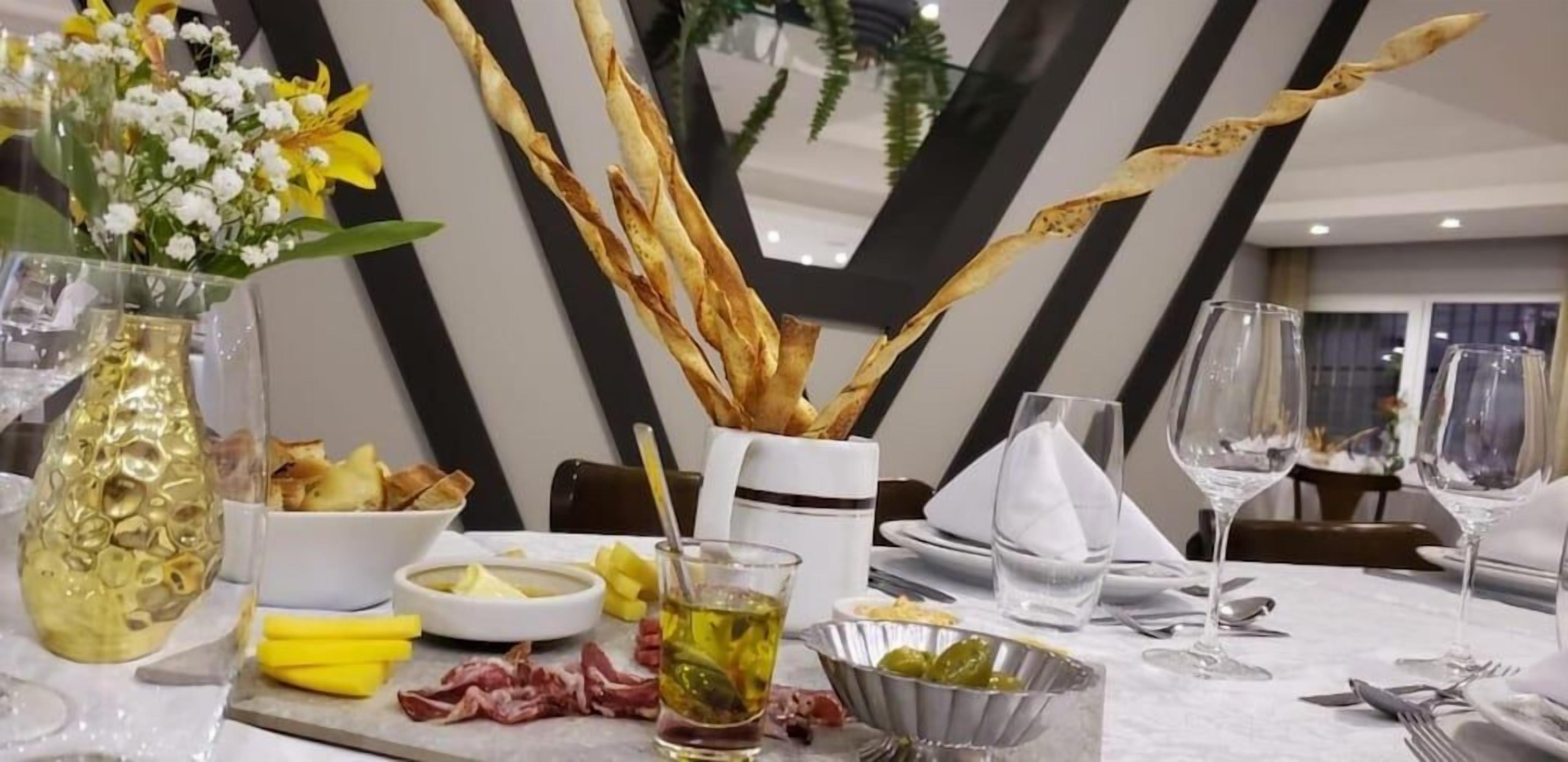 Mesa posta com pratos, talheres, um copo de bebida e um vaso com flores.