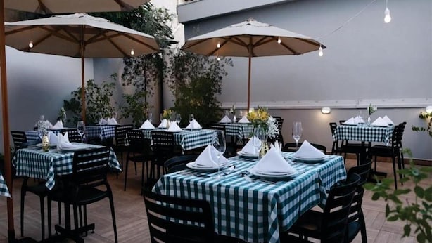 Un área de comedor al aire libre con mesas preparadas para dos, cubiertas por sombrillas y rodeadas de sillas.