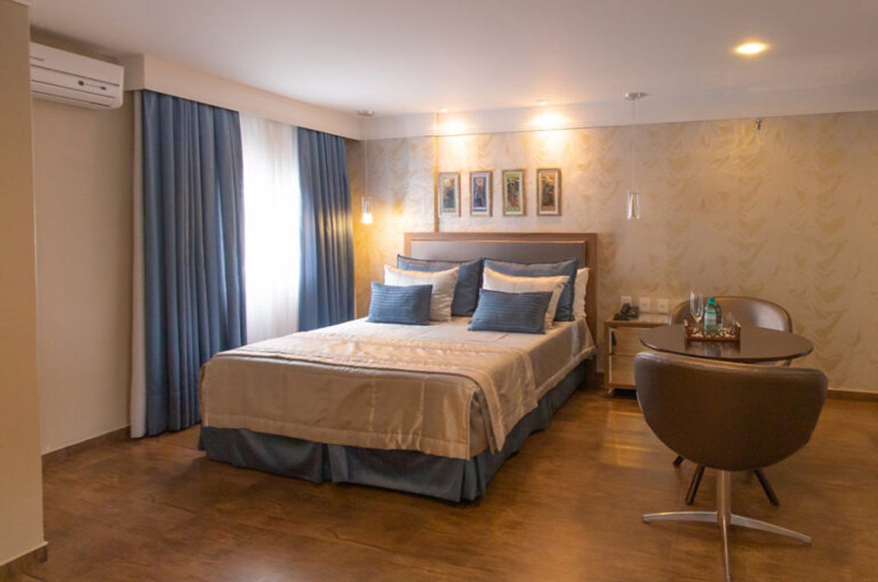 Quarto de hotel com cama, uma cadeira, uma mesa e ar condicionado fixado na parede.