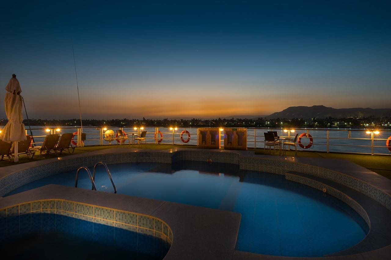A pool area with lounge chairs and a statue, overlooking a body of water and distant mountains.