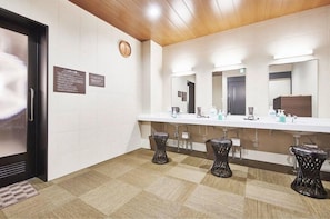 Um banheiro moderno com balcão extenso, várias pias e bancos pretos.