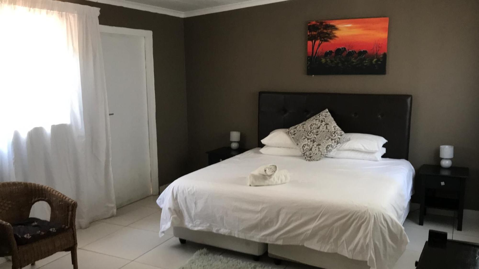 A bedroom with a bed, a chair, a nightstand, a painting, and a door.