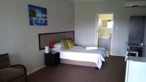 A hotel room with a bed, bedside tables, a chair, a desk, and a painting on the wall.
