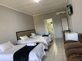 Habitación de hotel con tres camas, televisor, kitchenette pequeña y baño visible a través de una puerta abierta.