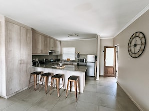 A modern kitchen with a central island, bar stools, and a clock on the wall. - Nemesia Court (Cape Town)