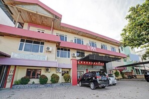 A multi-story building with a sign reading 'Kuta Karang Baroe.' There are several parked cars in front, and the building has multiple windows and air conditioning units. - OYO 90487 Wisma Kuta Karang Baru (Lhokseumawe)