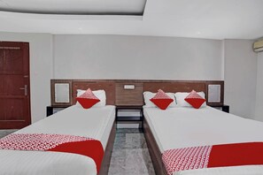 Habitación de hotel con dos camas, cabecero de madera, mesita de noche y colcha estampada en rojo y blanco.