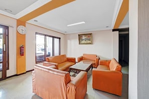 A hotel lobby with orange leather sofas, a coffee table, a clock, and a painting on the wall.